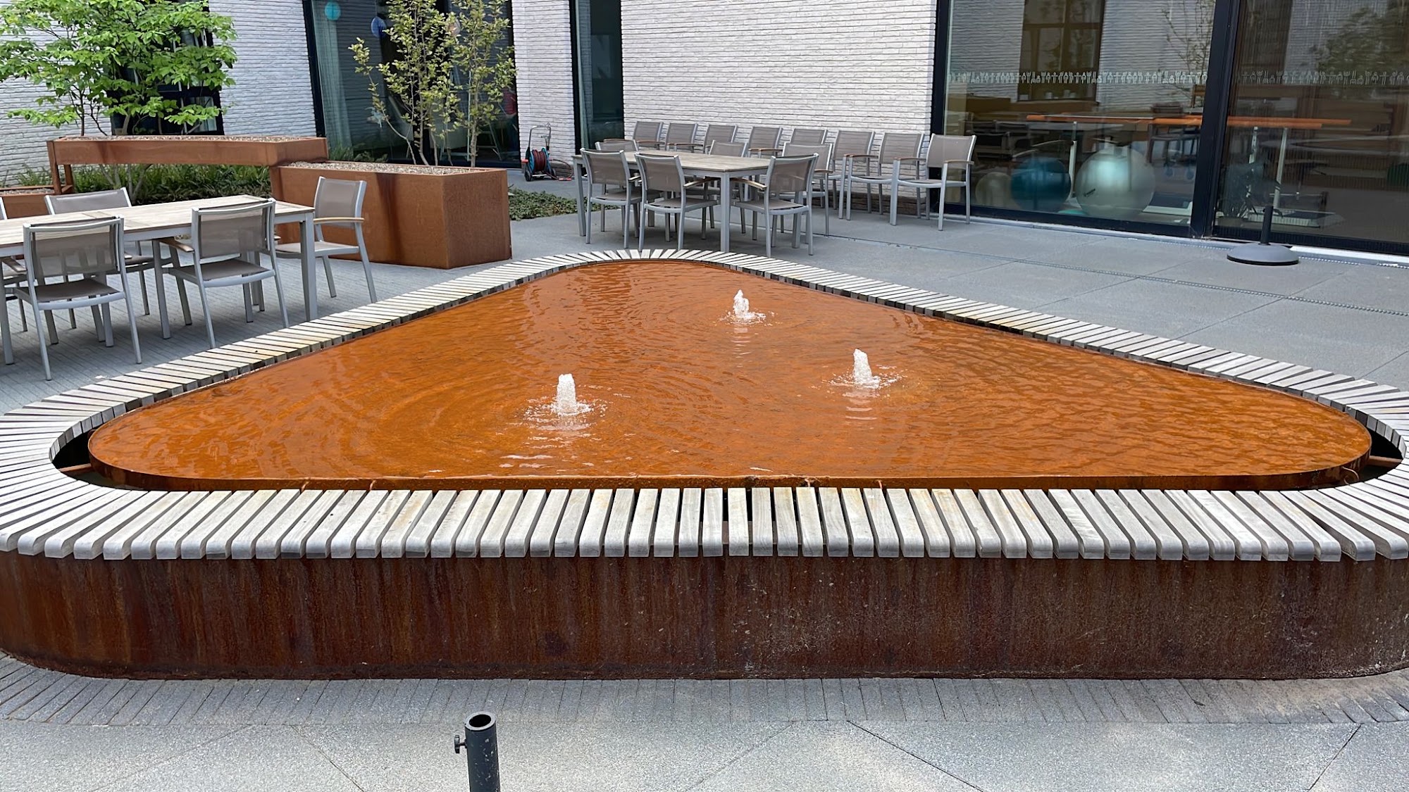 Driehoekige cortenstalen watertafel met houten zitrand bij een woonzorgcentrum in Rumst