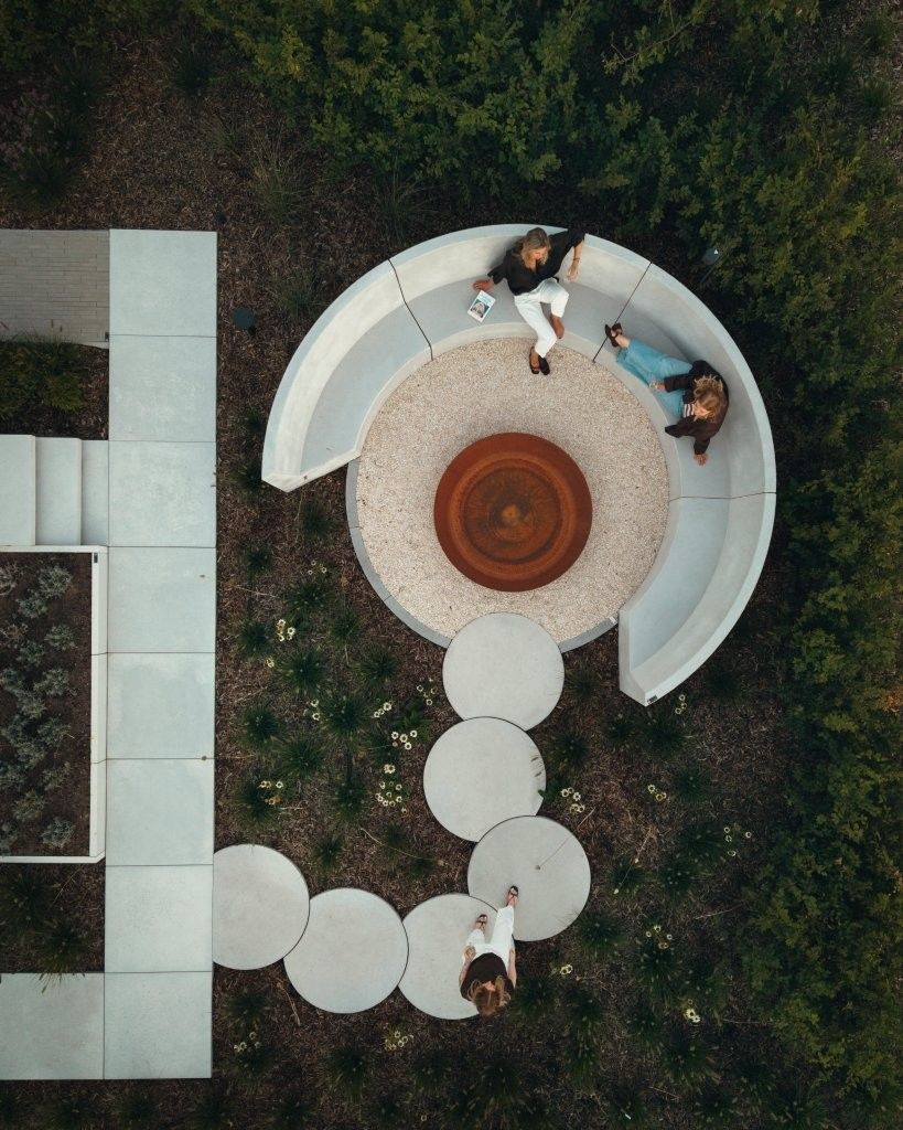 Vue aerienne d'un cercle de banquettes en beton autour d'un brasero Diablo en acier corten, jardin Outspiration d'Ebema