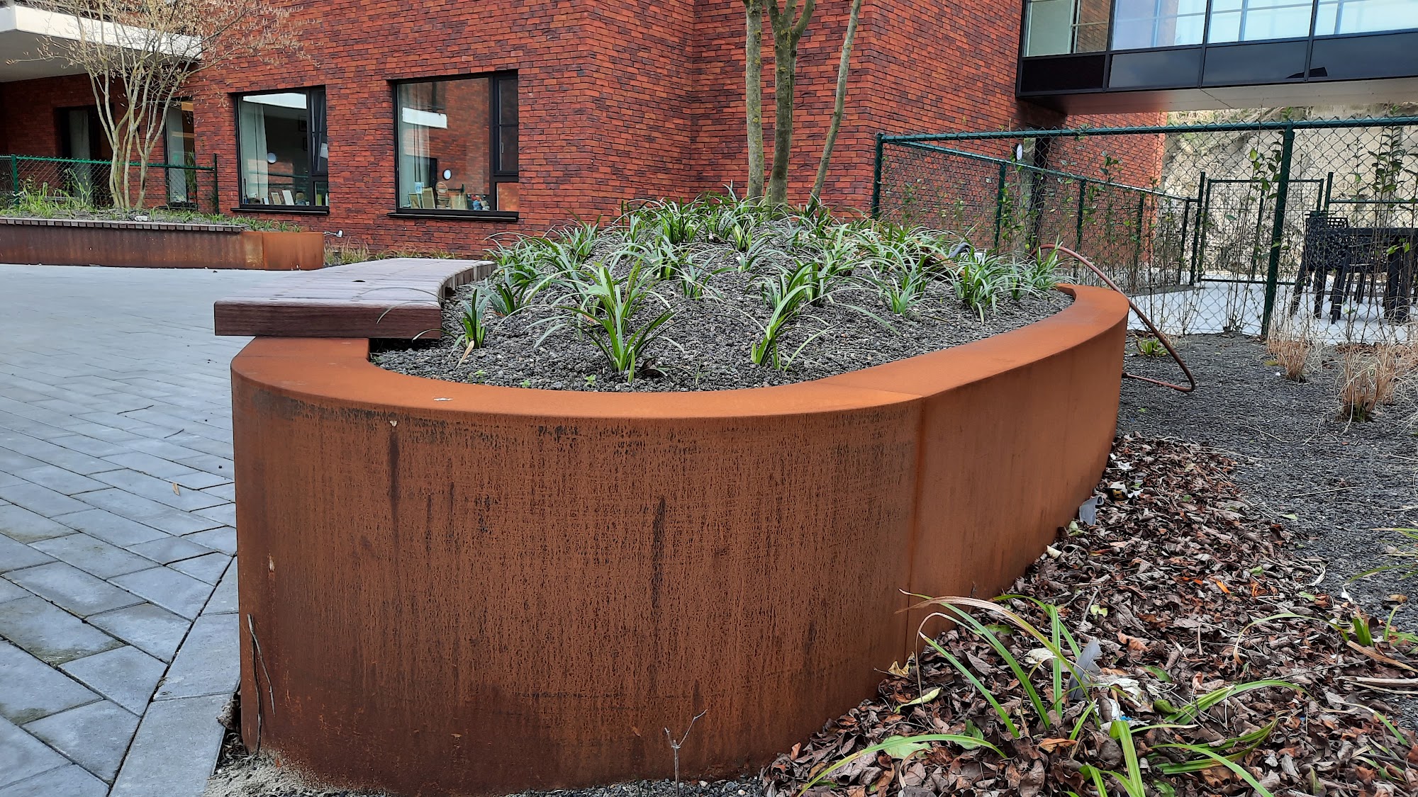Ovale cortenstalen plantenbak met houten zitrand op het binnenplein van woonzorgcentrum Populierenhof