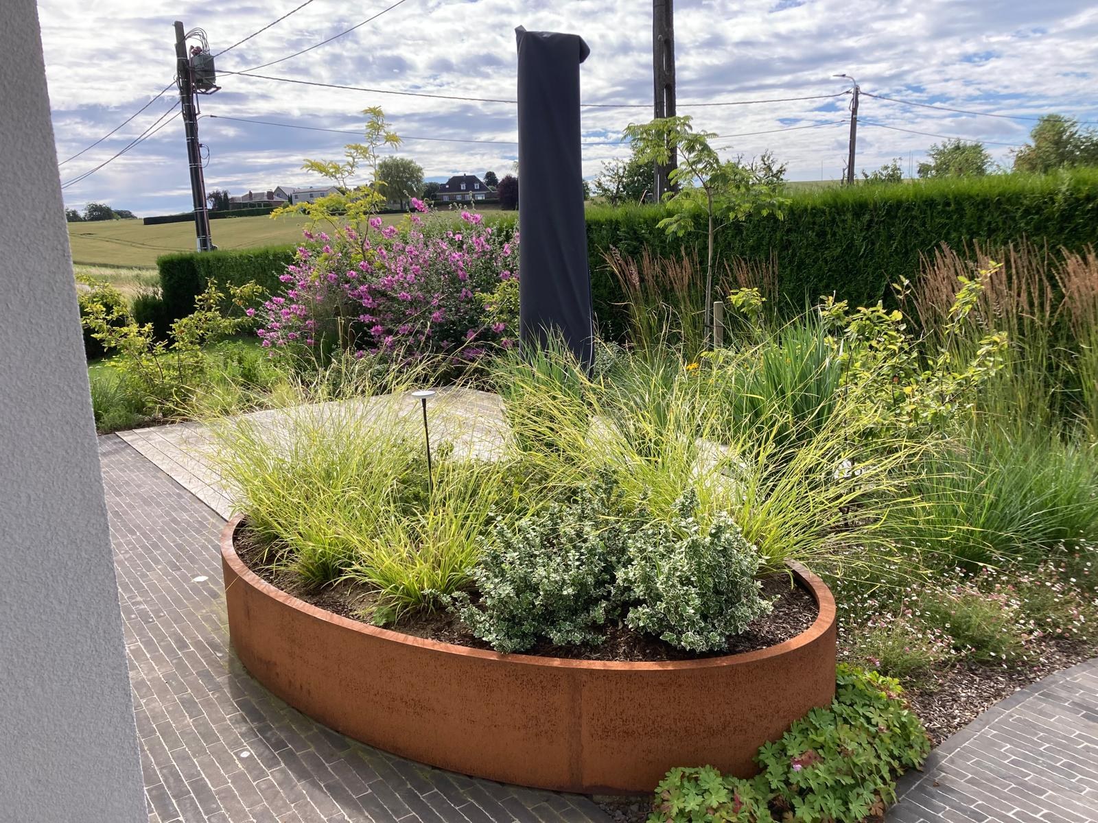 Bac à plantes ovale en acier Corten avec graminées ornementales dans un jardin