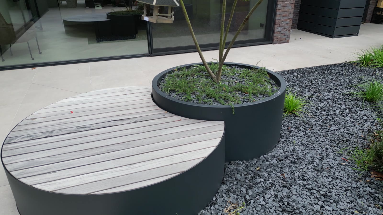 Ronde aluminium plantenbak met houten zitbank op het terras