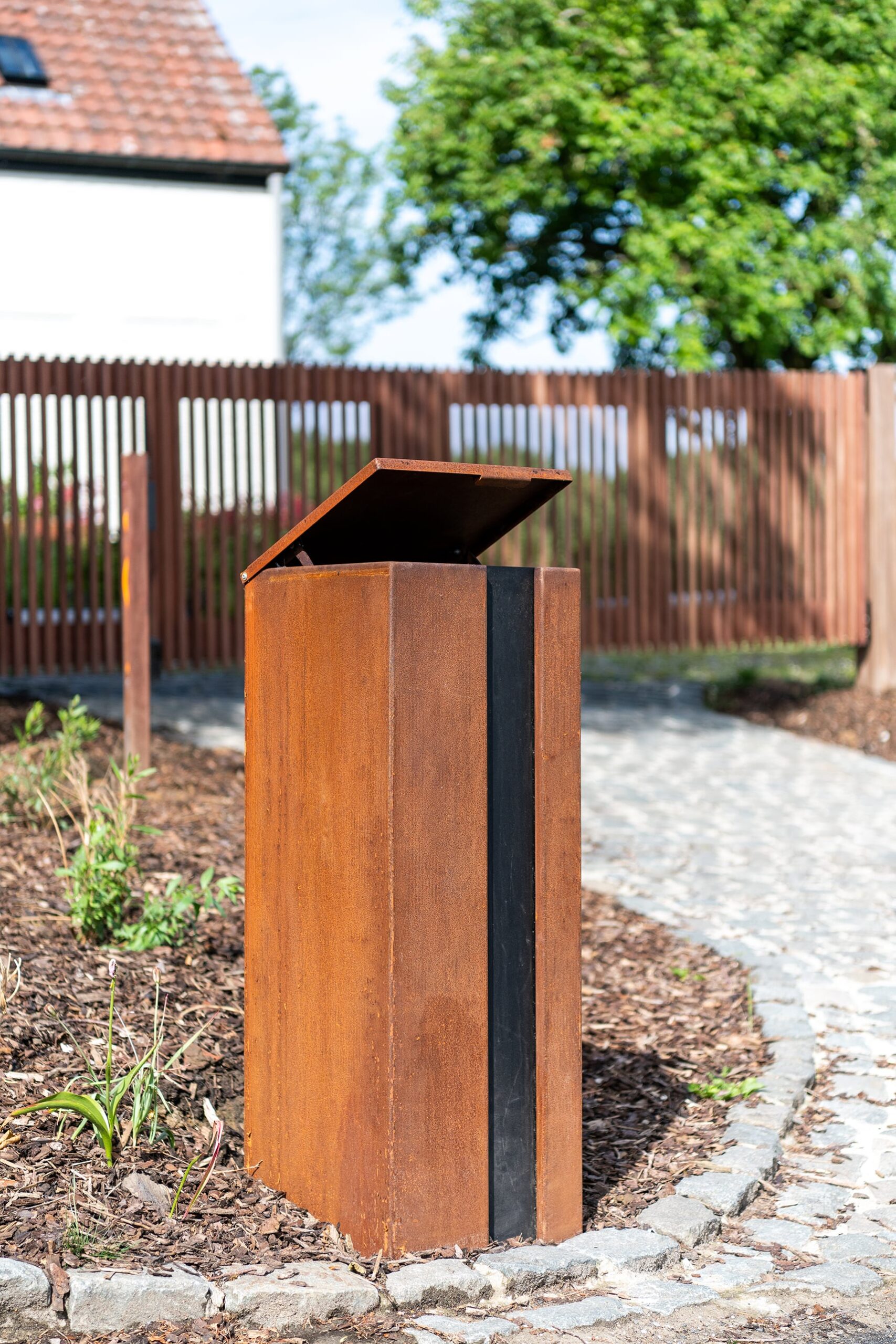 Corten steel mailbox with a black accent strip in a garden